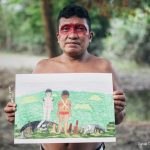 Joseca Yanomami segurando uma obra de sua autoria. (Reprodução)