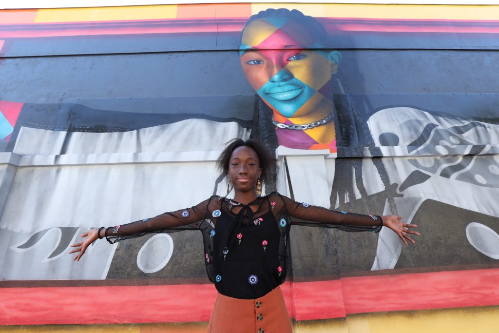 Priscilia, da Libia, de braços abertos na frente de seu mural 